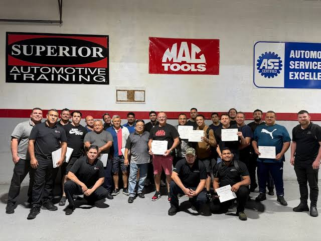 Class of technicians holding their certificates in front of the Superior Automotive Training sign
